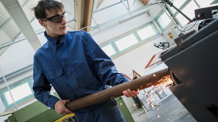 Auszubildender bearbeitet ein Metallteil an einer Maschine