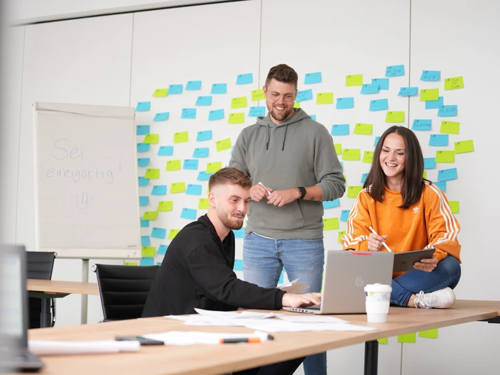 Teambesprechung zwischen drei jungen Mitarbeitenden 